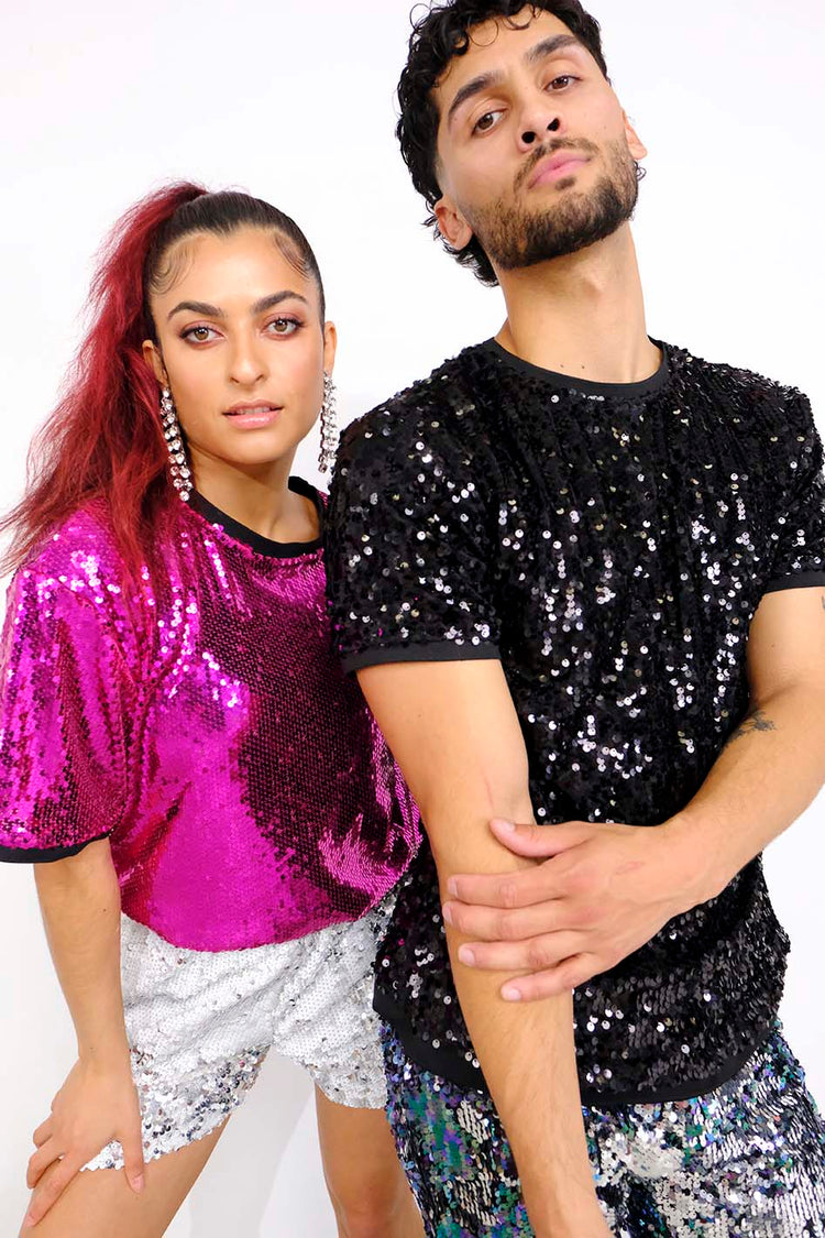 man wearing black sequin t-shirt and purple blue sequin shorts as part of a rave outfit for men. Woman wearing pink sequin t-shirt and white silver sequin shorts as part of a festival outfit for women