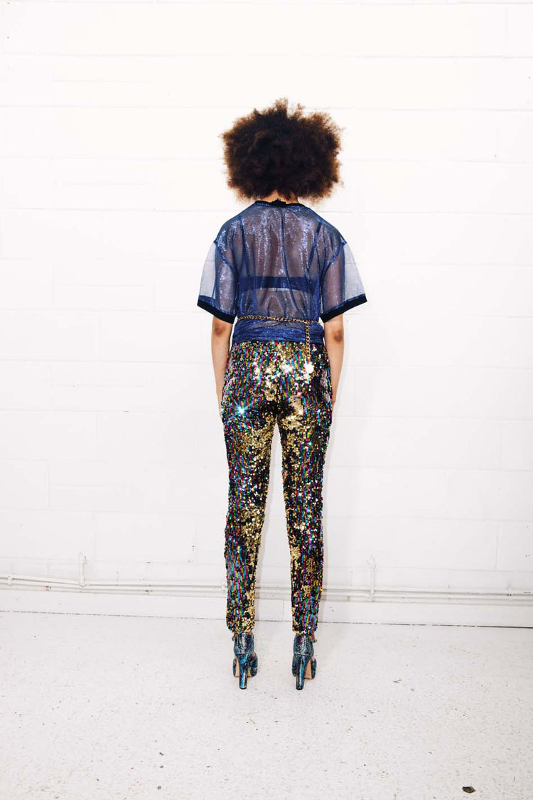 Woman wearing rainbow sequin pants and sheer blue top for festival outfit